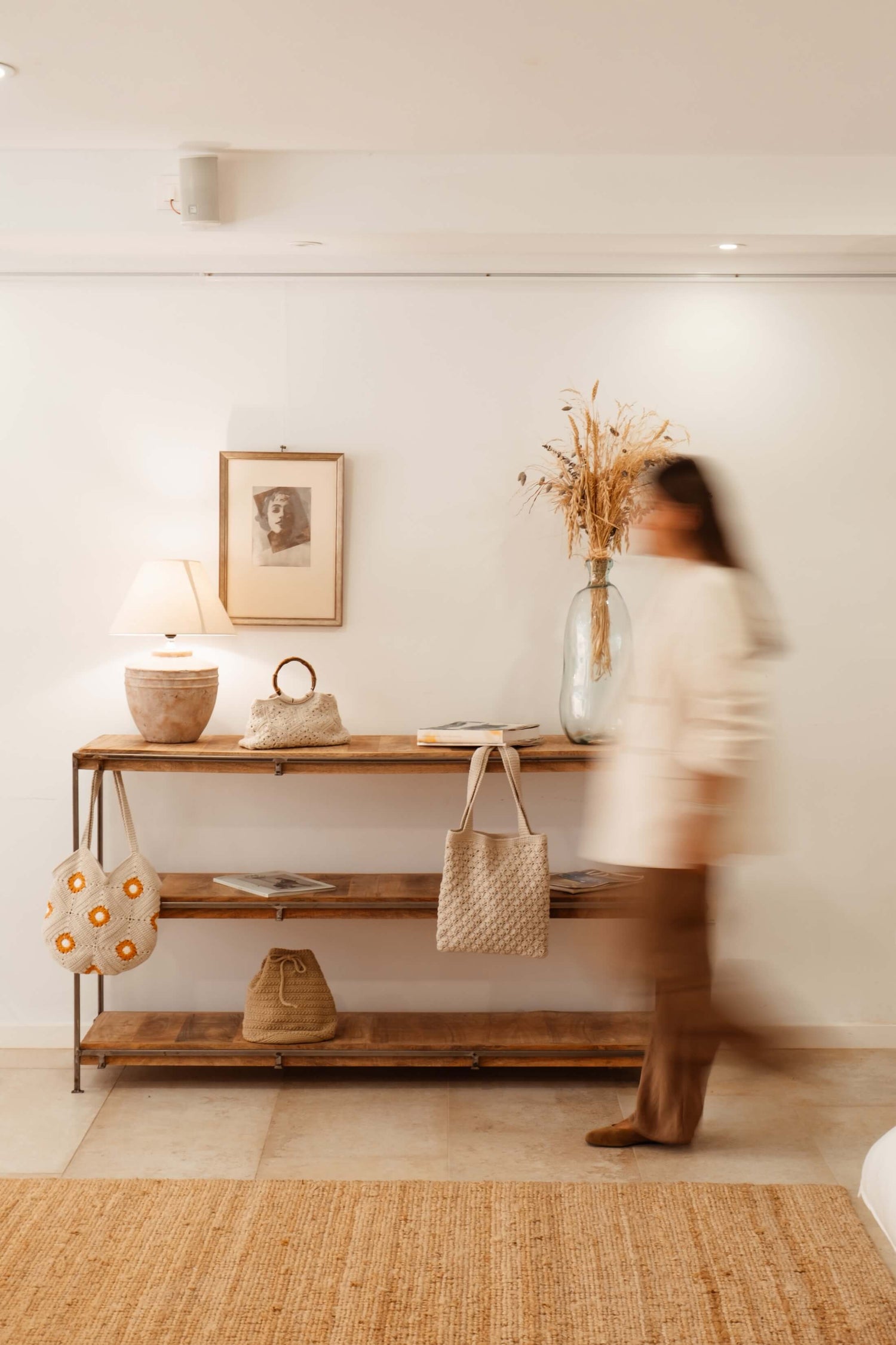 Mujer caminando junto a estantería decorativa con bolsos de crochet Cabori en ambiente mediterráneo y artesanal.