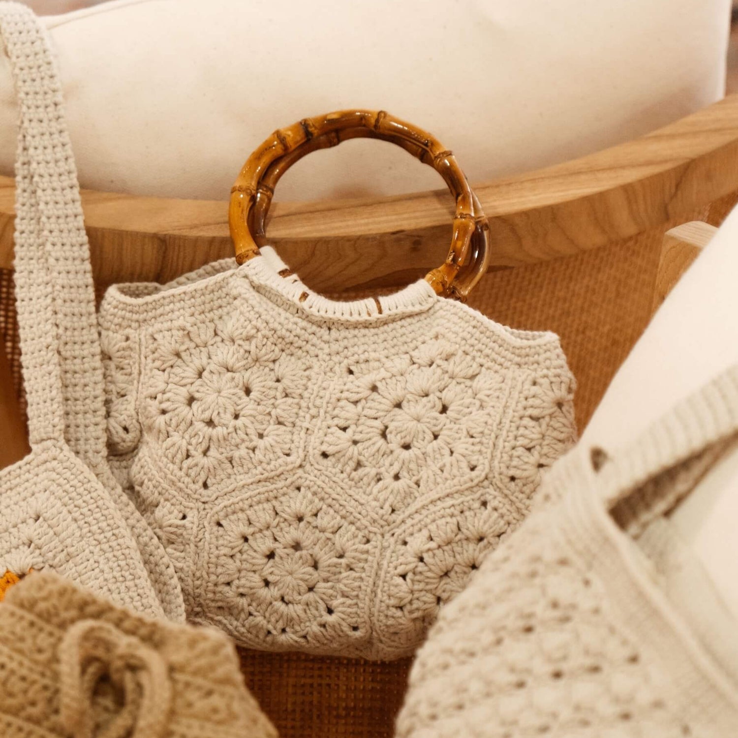 Primer plano del bolso BRUMA de Cabori, tejido a mano en crochet beige con patrón floral, rodeado de otros bolsos de Cabori.