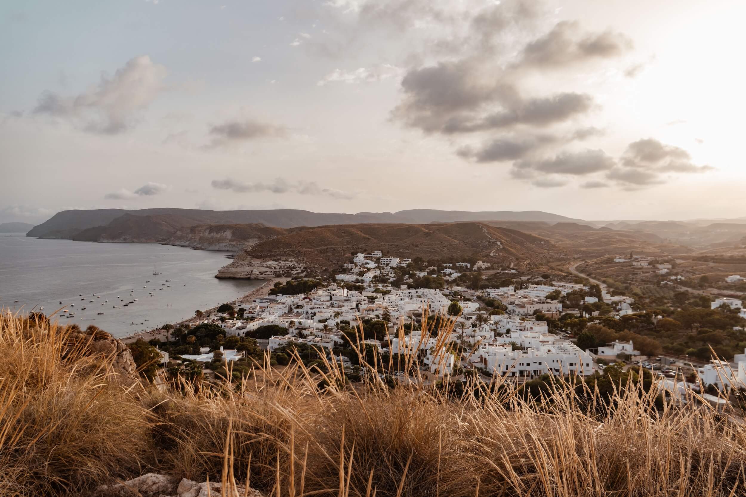 Vista panorámica del Cabo de Gata al atardecer con casas blancas, mar y paisaje natural en tonos cálidos.