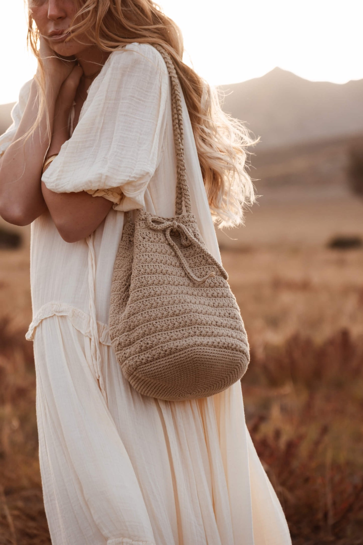Mujer con bolso CALIMA tipo bombonera en entorno natural, diseño artesanal inspirado en el Cabo de Gata